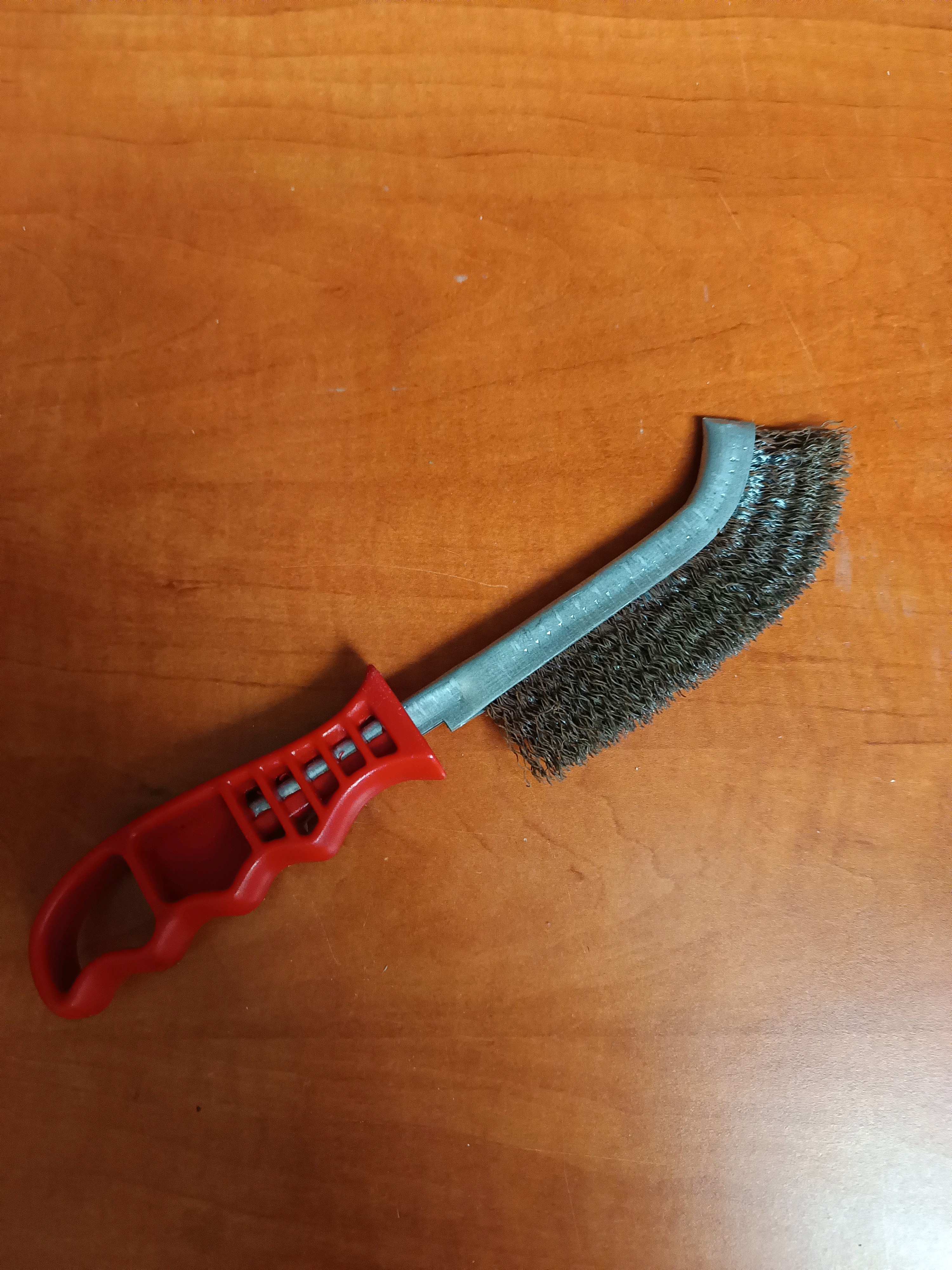 Brosse métallique courbe à manche plastique rouge